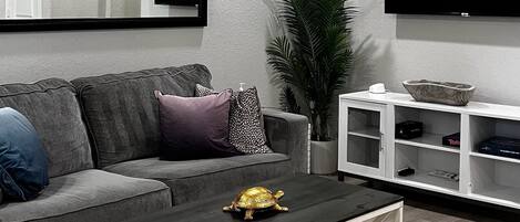 A modern living room with a ceiling fan, a flat-screen TV, a sofa, a coffee table, and a plant.