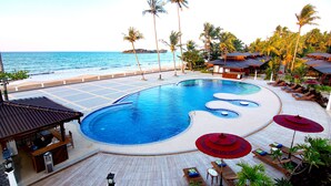 Uma área de piscina com design curvo, cadeiras de descanso, guarda-sóis e vista para o oceano.