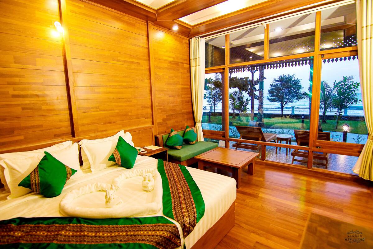 Una habitación de madera con una cama, una mesa y vistas a un jardín a través de amplios ventanales.
