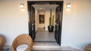 Un pasillo de diseño moderno, con un marco de puerta negro, dos luces empotradas en la pared y una planta de cactus.