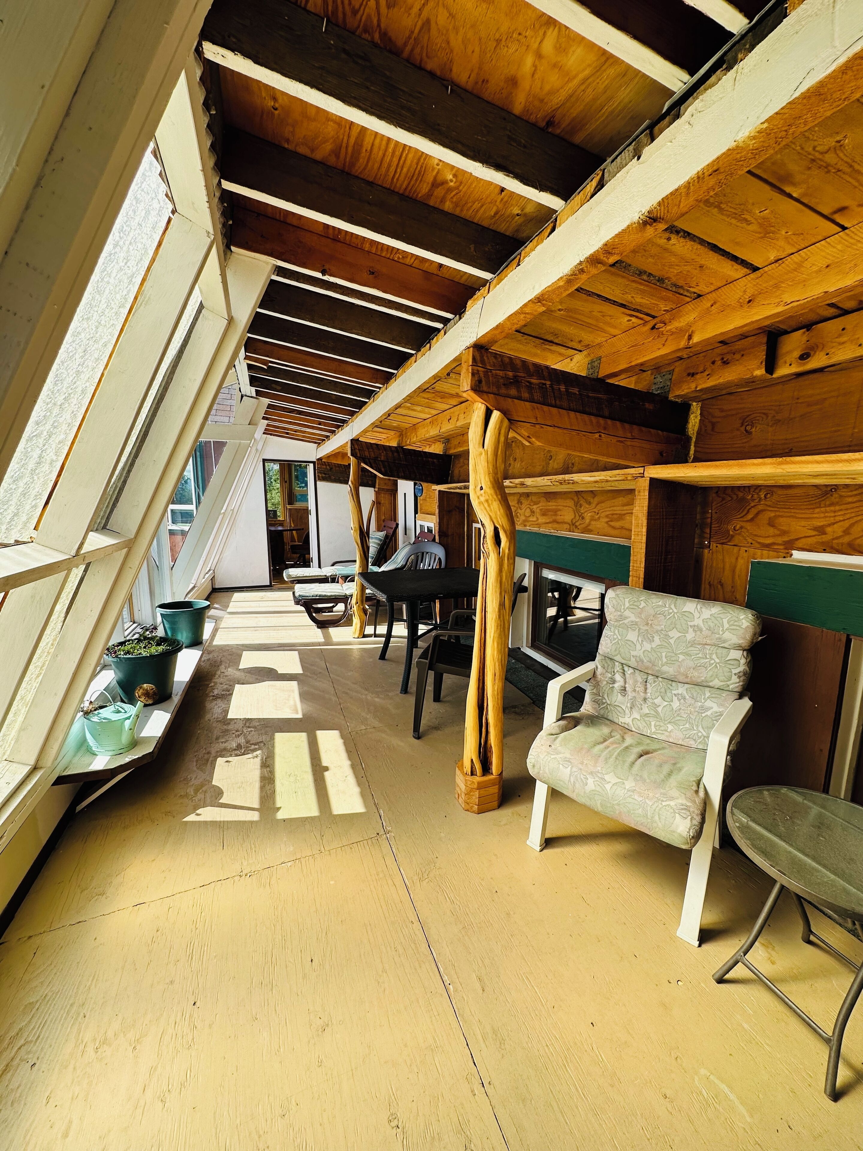 A room with a sloped ceiling, wooden beams, a green cushioned chair, a table, and potted plants.
