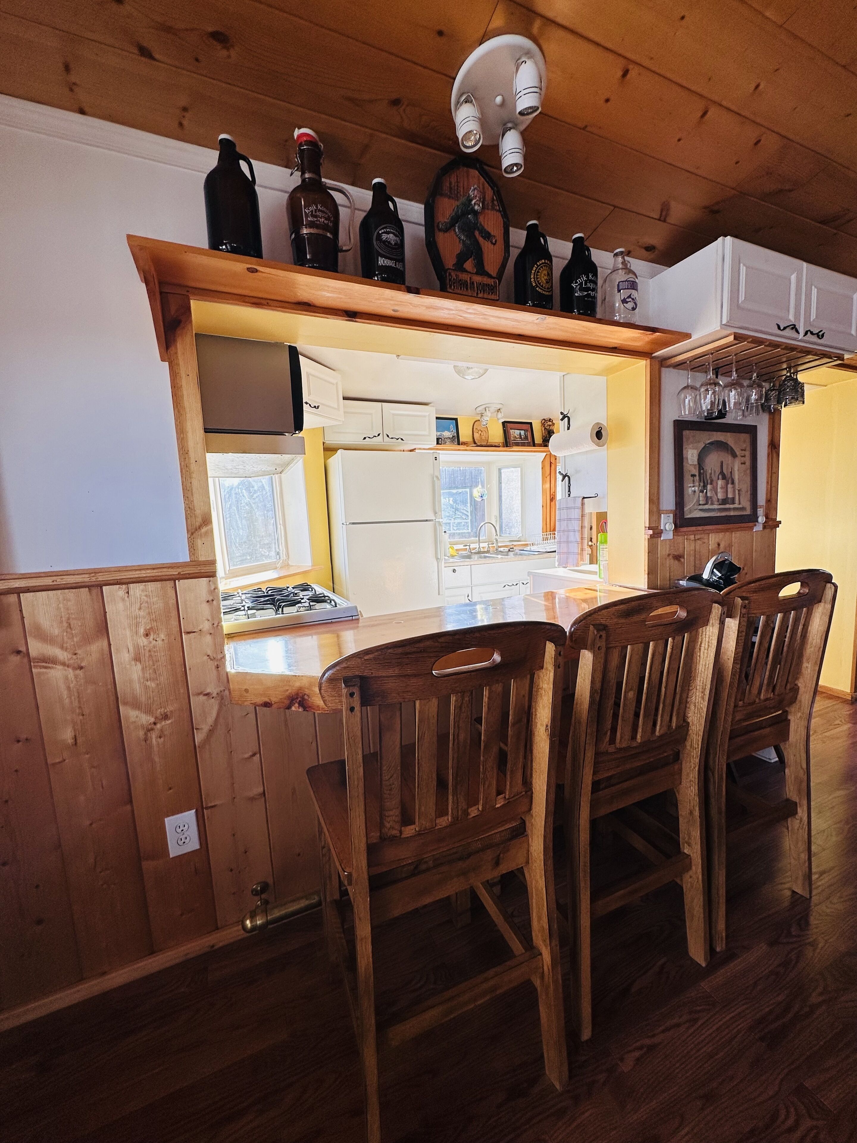 Una cocina con armarios de madera, una isla integrada con taburetes de bar y varias botellas en el estante superior.