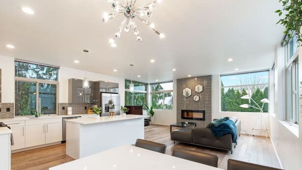 A modern kitchen with a central island, a dining area with a white table, and a living room with a sofa and a fireplace. - Luxe 3Bdr Home | Parking | Roof Oasis | City Views (Seattle)