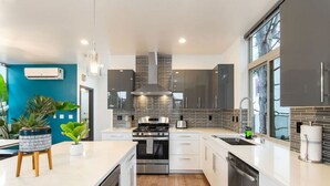 A modern kitchen with white cabinetry, a central island, a built-in oven, and a large window providing natural light. - Luxe 3Bdr Home | Parking | Roof Oasis | City Views (Seattle)