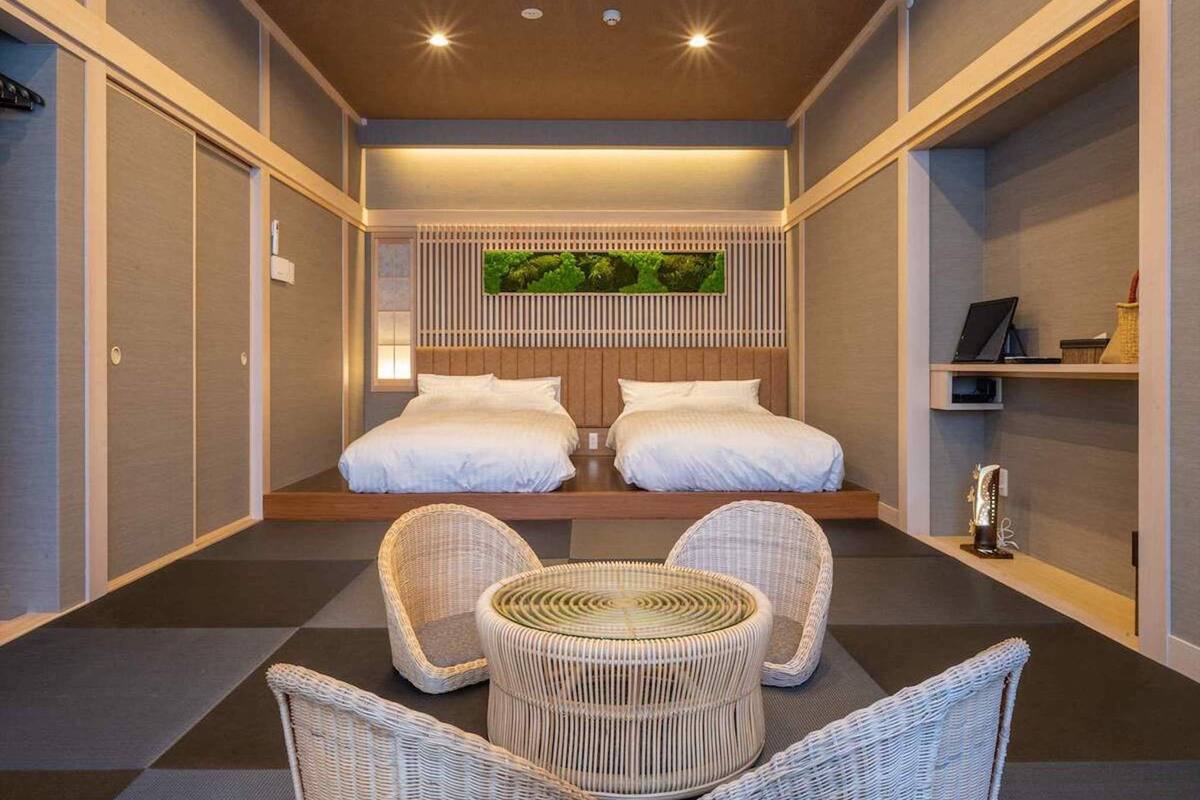 Une chambre d’hôtel moderne avec un grand lit, deux oreillers blancs, une table ronde en osier et des chaises en osier.