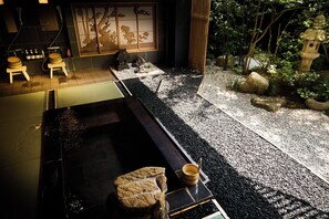A traditional Japanese-style interior with tatami flooring, a low table, and a small garden area with rocks and a water feature.