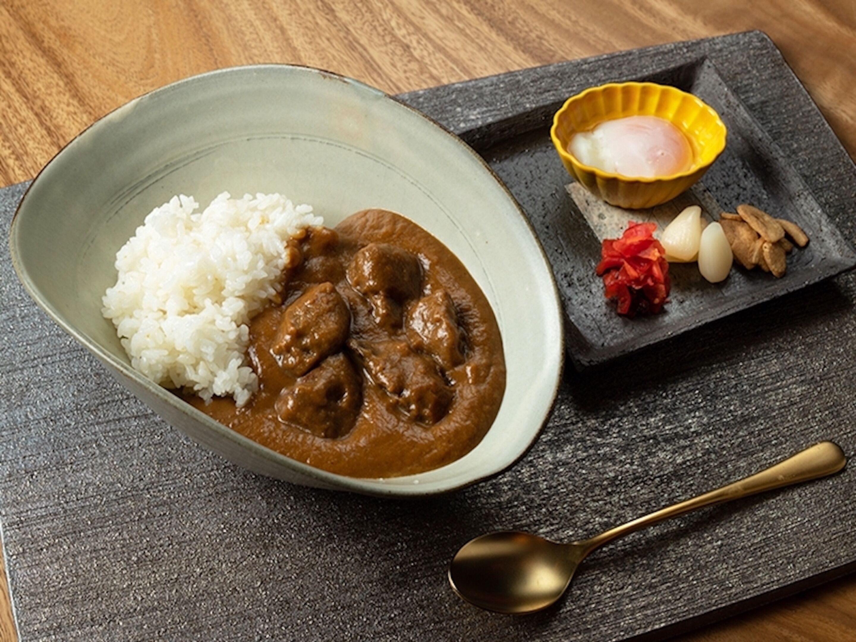 Un tazón de arroz blanco y curry con una cuchara sobre un plato de pizarra oscuro.