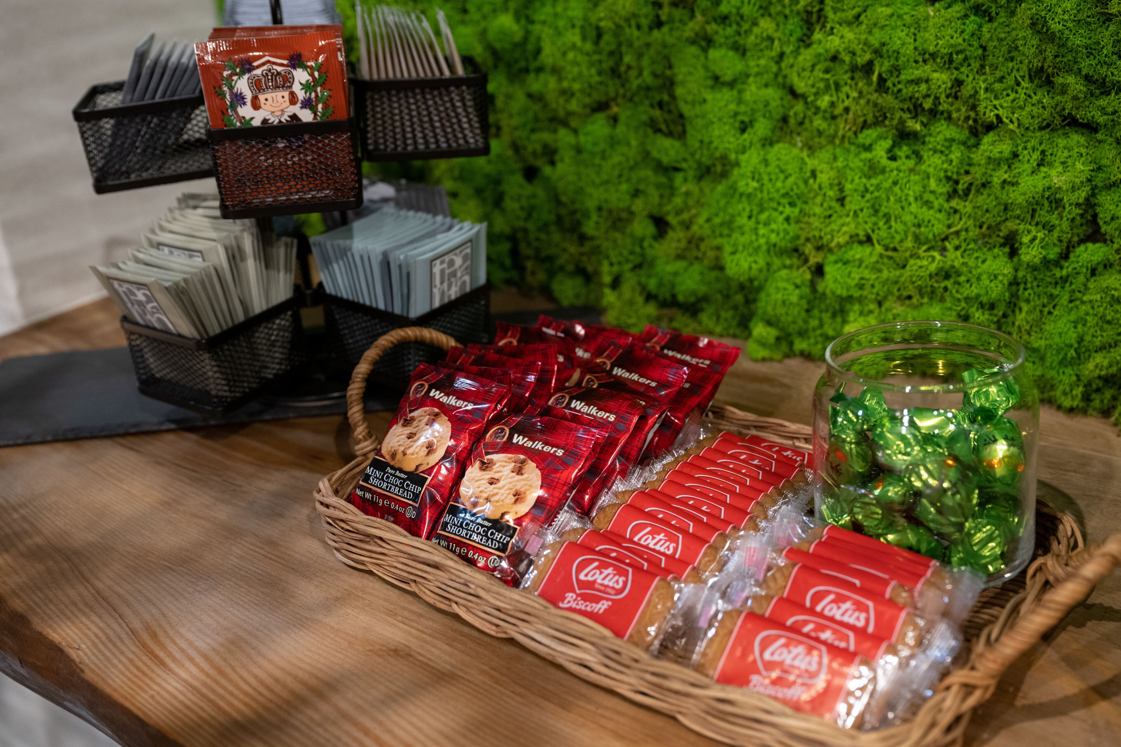A table with baskets of snacks, including Walkers and Lotus Biscuits, and a glass jar of green candies.