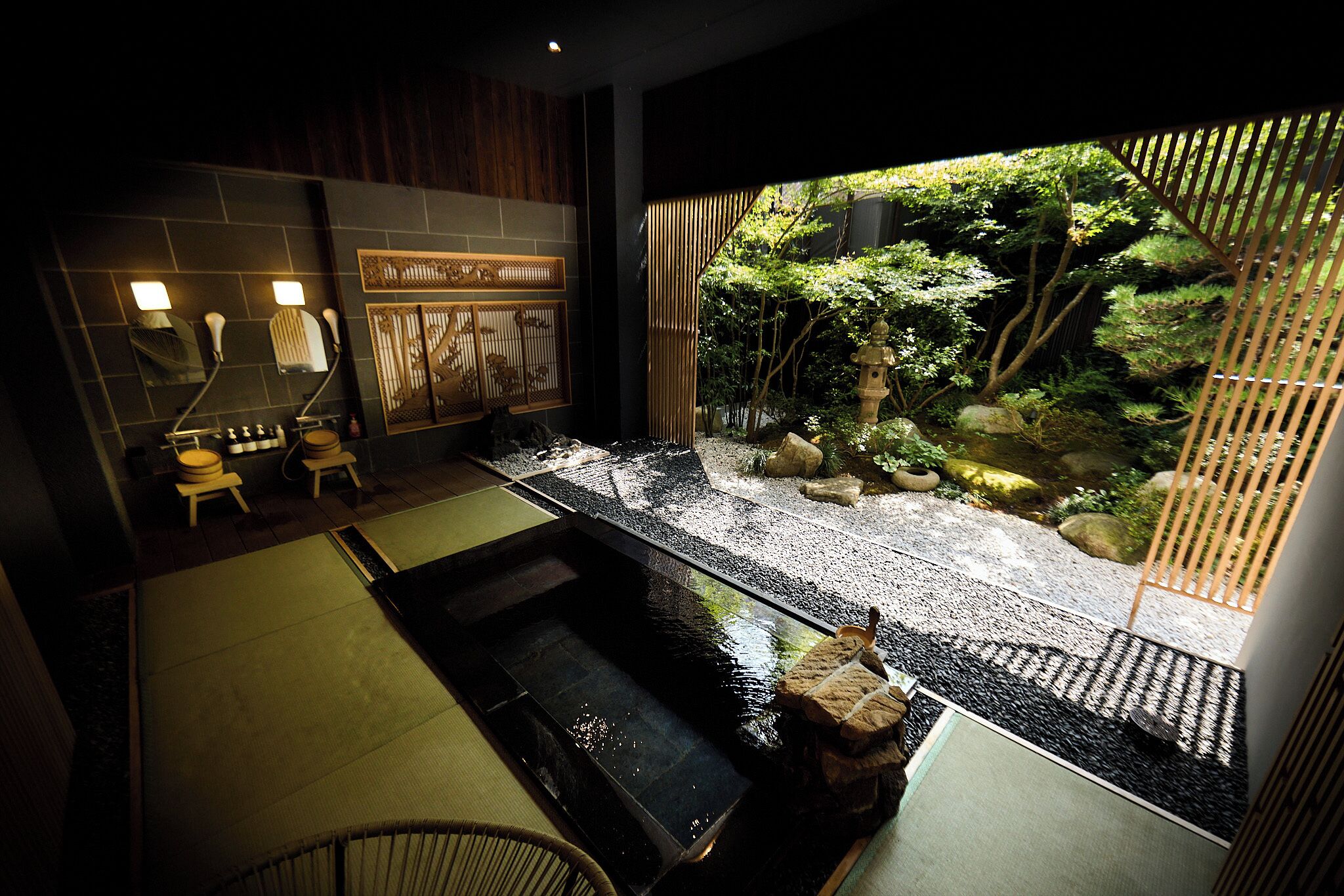 A traditional Japanese-style bathroom with a small indoor garden, a stone hot tub, and a bamboo screen.