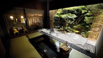 A traditional Japanese-style bathroom with a small indoor garden, a stone hot tub, and a bamboo screen.