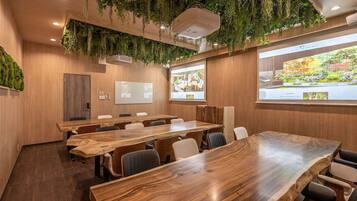A conference room with wooden tables and chairs, a whiteboard, and a projector screen displaying a presentation.