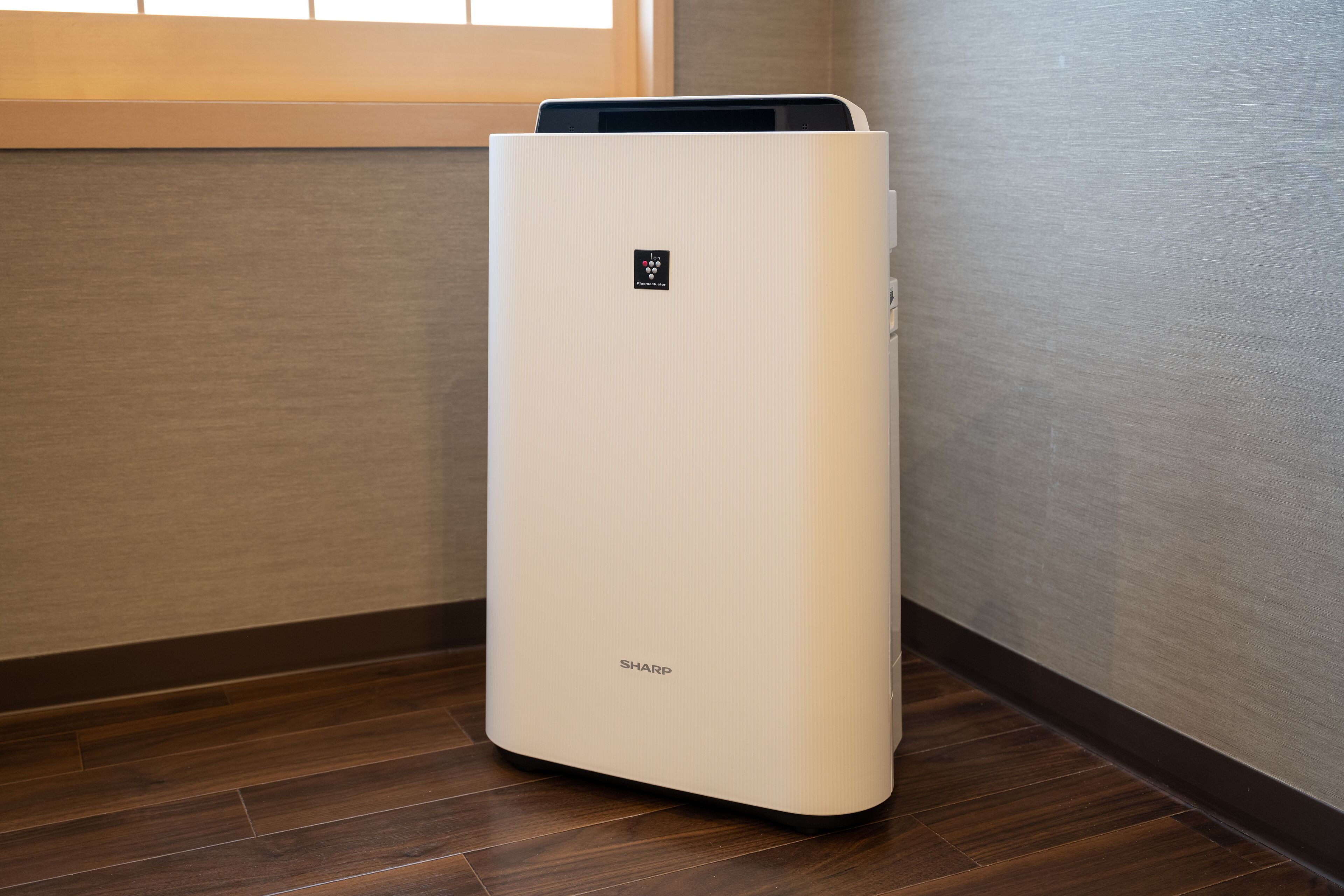 A white air purifier with the brand name 'SHARP' on a wooden floor.