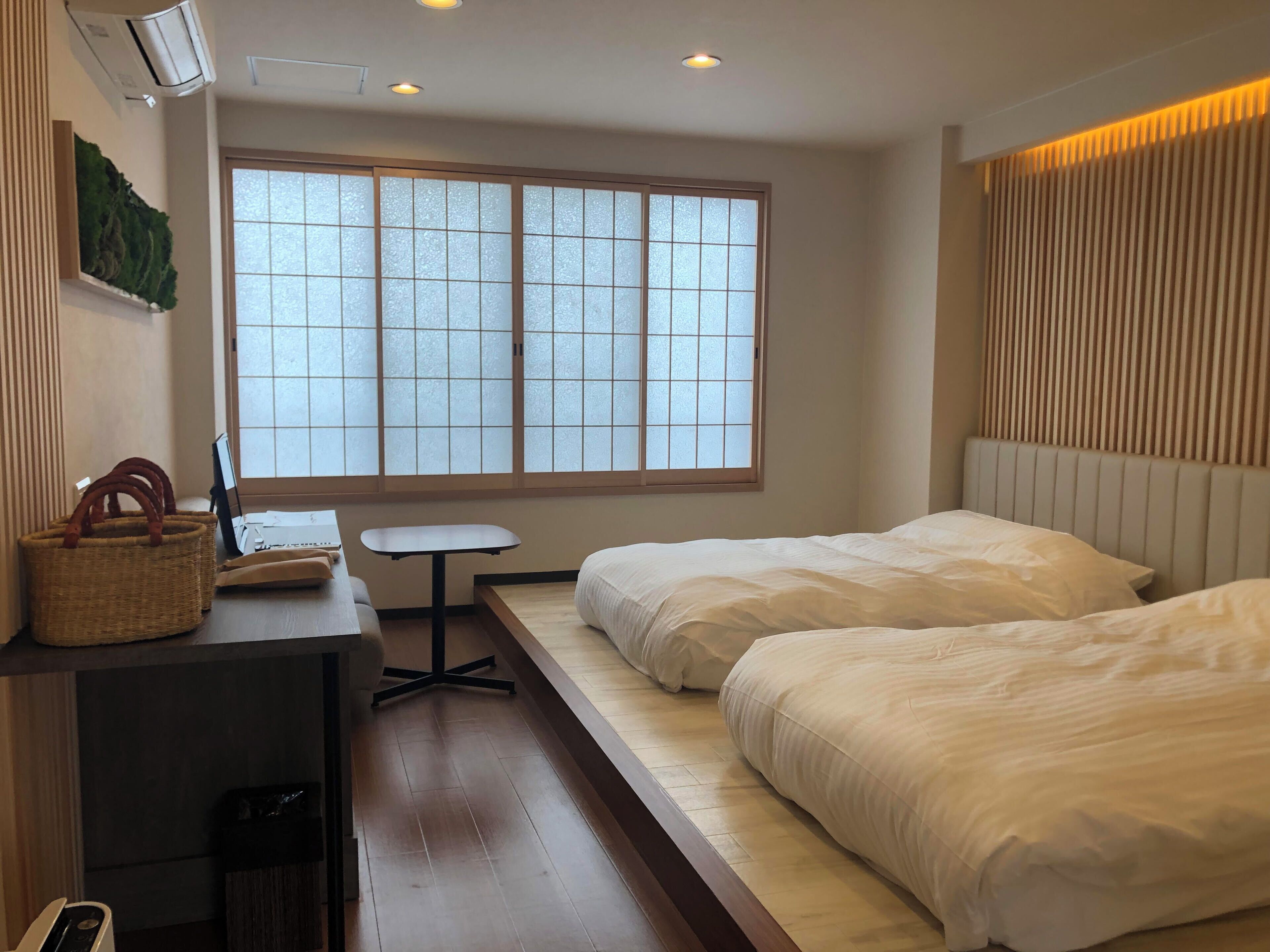 Ein Hotelzimmer mit einem Bett, einem Schreibtisch mit Stuhl, einem kleinen Tisch und einem Fenster mit Milchglas.