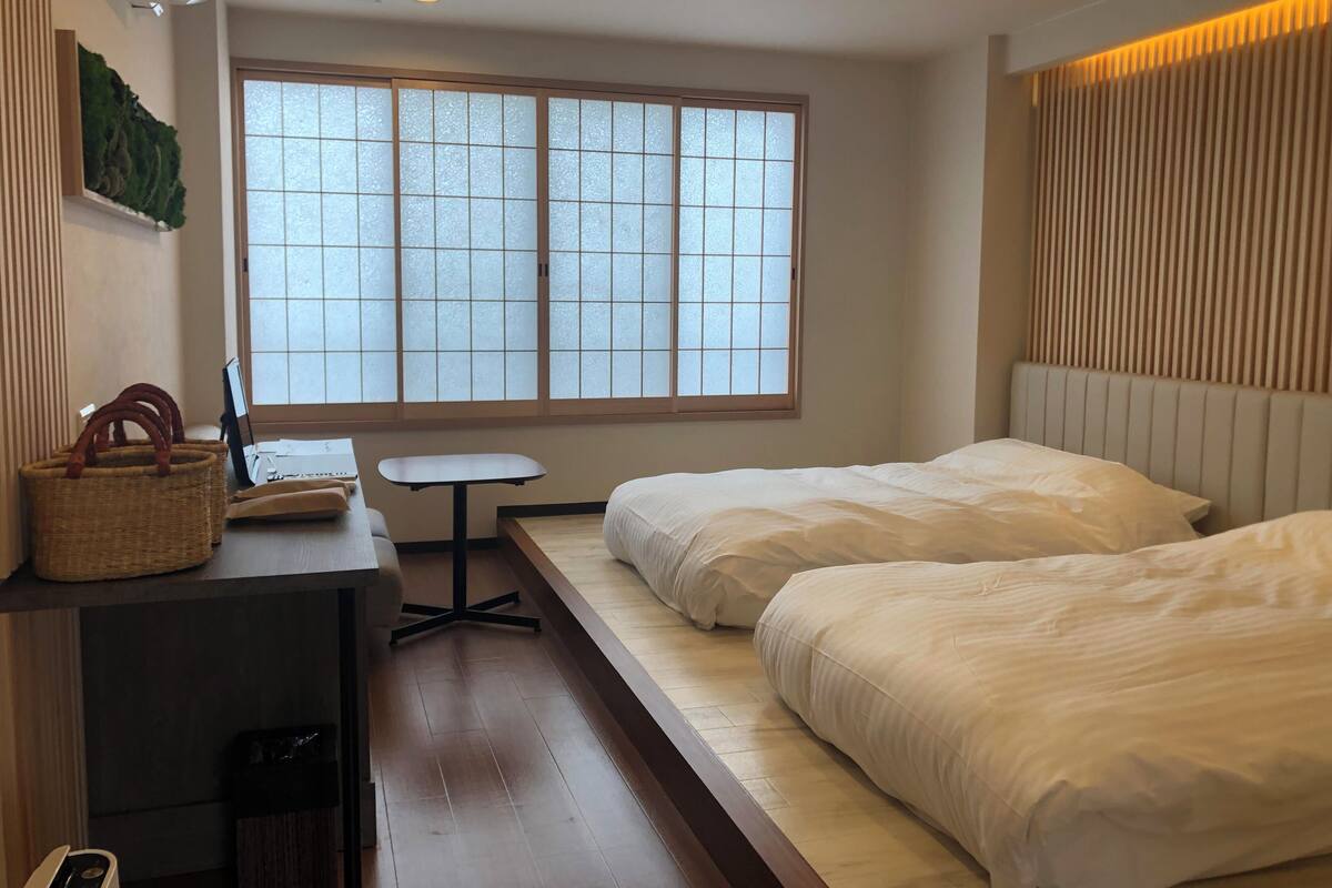 Une chambre d’hôtel comprenant un lit, un bureau avec une chaise, une petite table et une fenêtre avec des panneaux en verre dépoli.