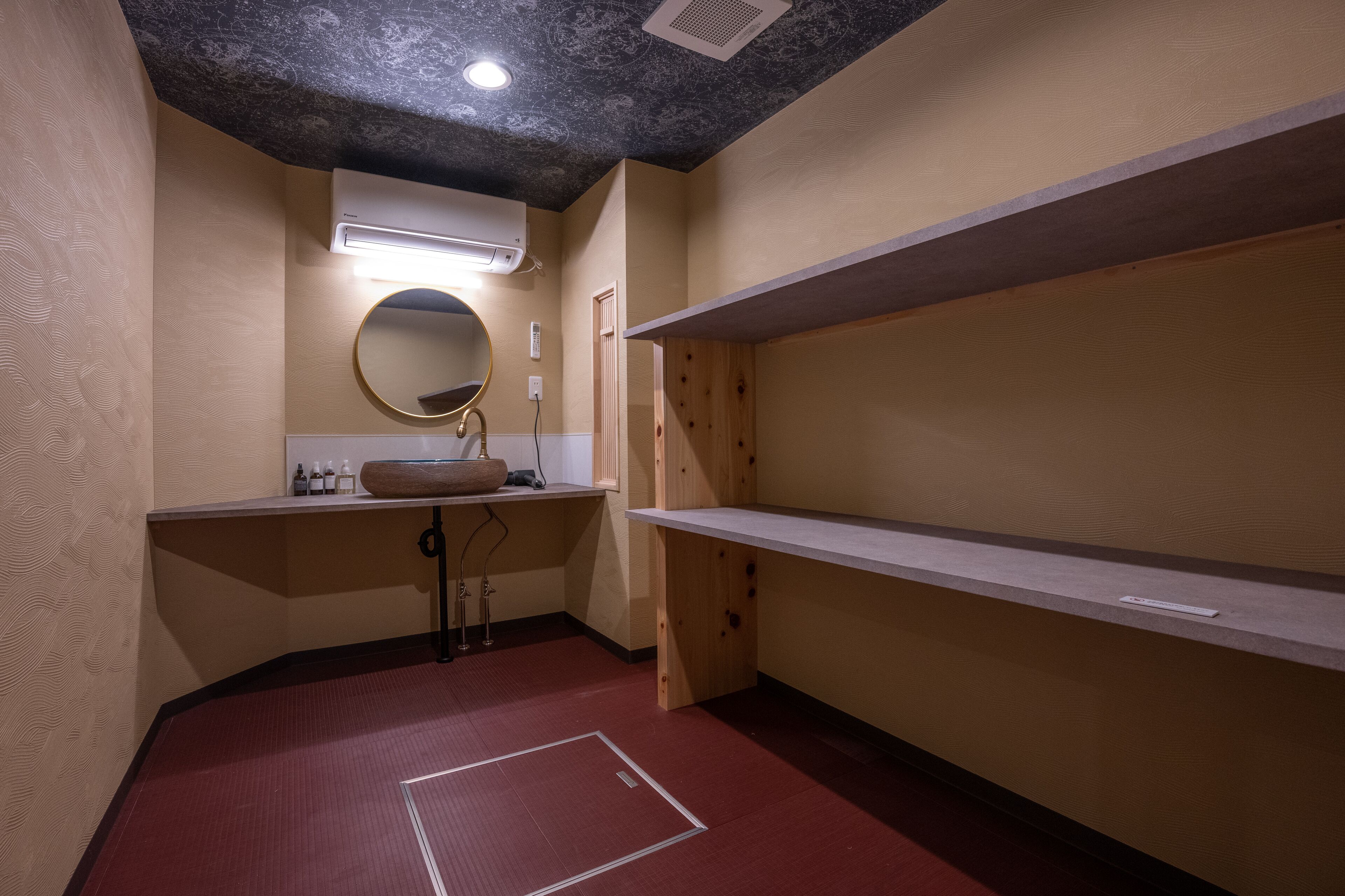 Un baño pequeño y funcional con un espejo redondo, un lavamanos y estantes de madera.