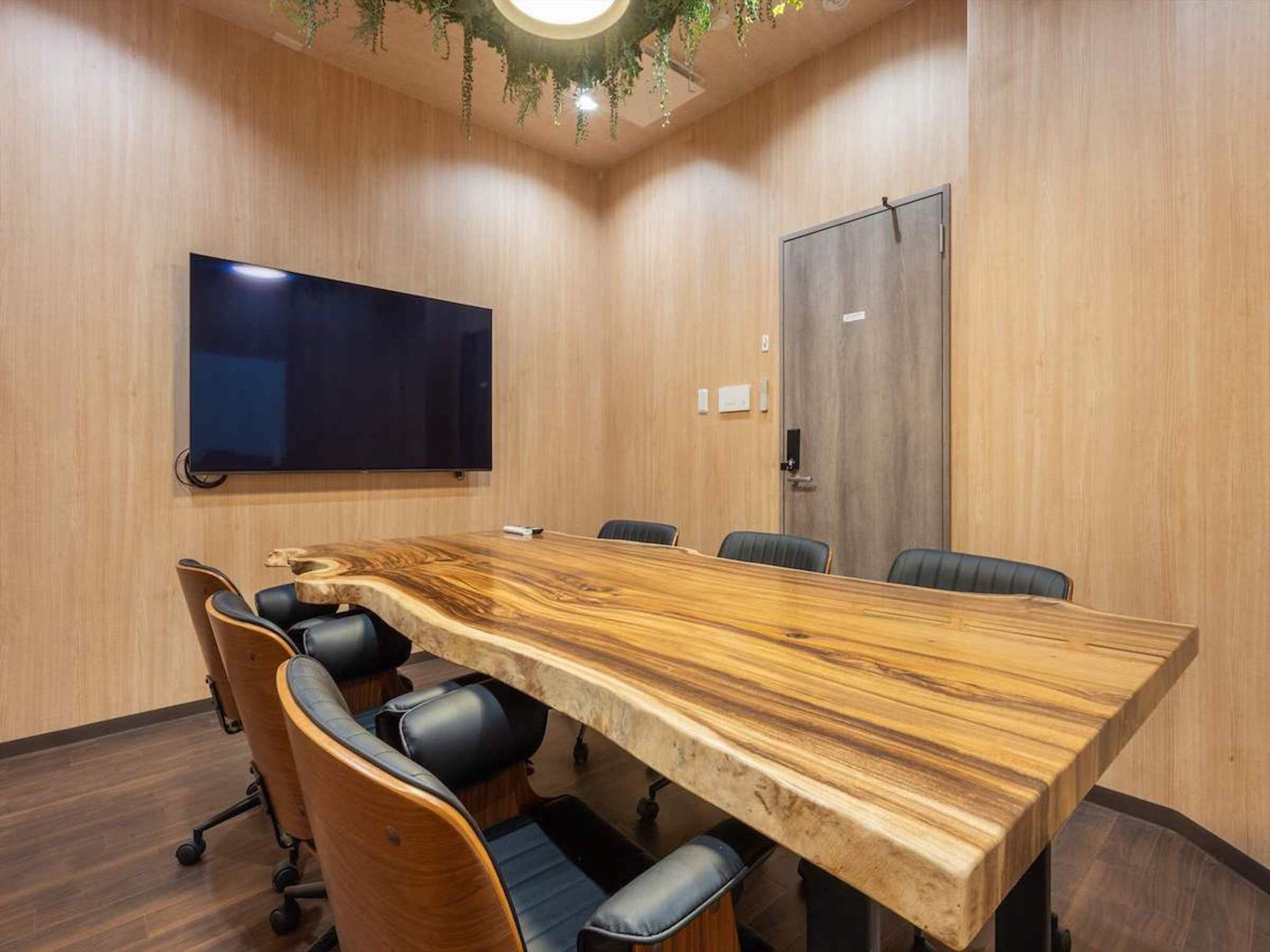 Un salón de conferencias con una amplia mesa de madera, sillas de cuero negro, un televisor de pantalla plana y una puerta con cerradura.