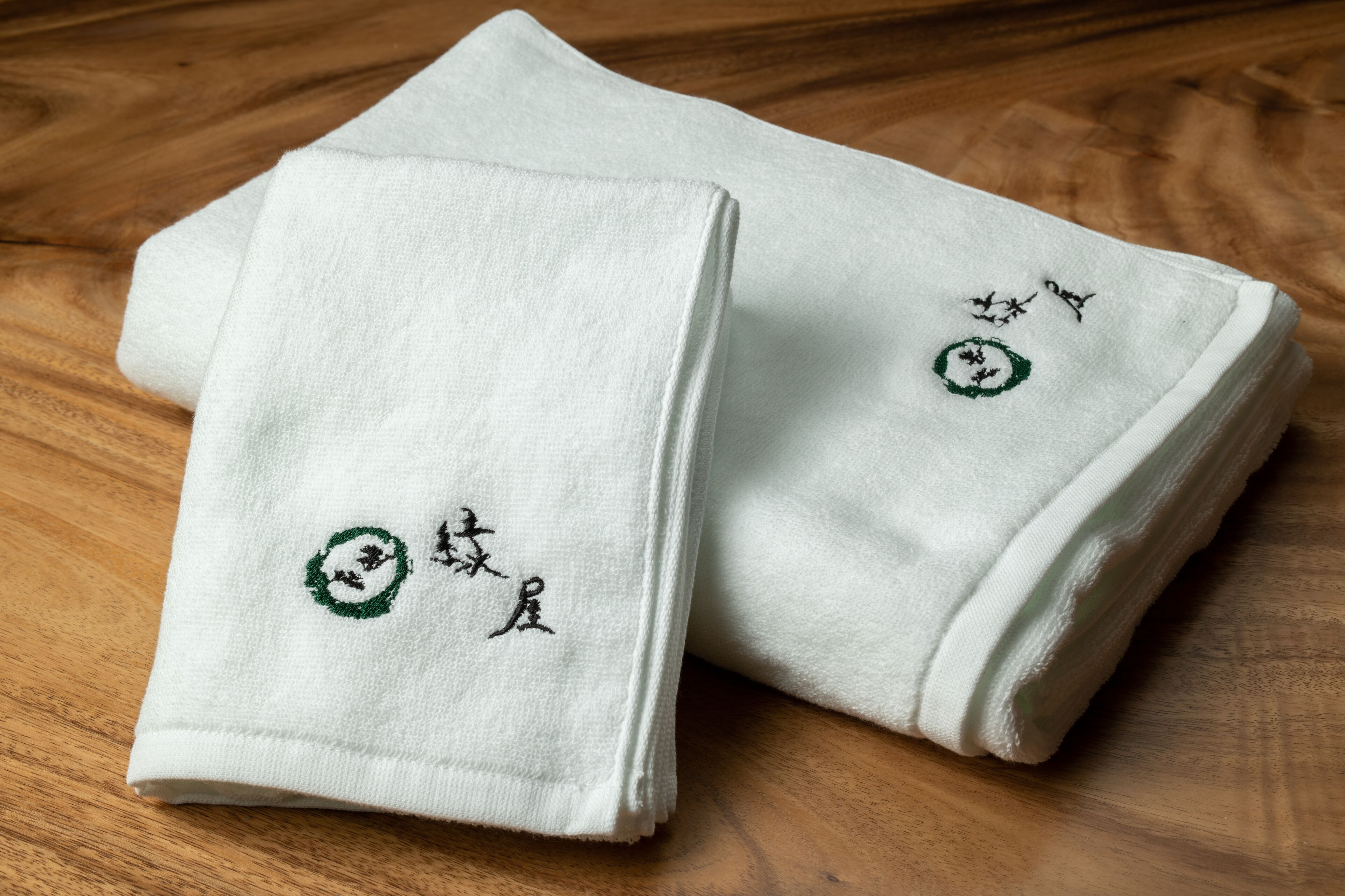 Two folded white towels with embroidered designs on a wooden floor.