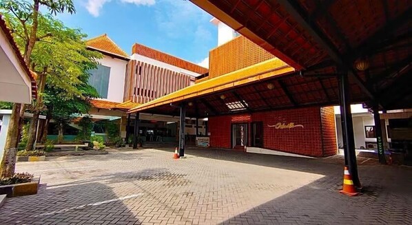 A building with a covered entrance, a brick facade, and a sign with a logo. - Odaita Hotel (Pamekasan)
