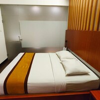 Una cama individual con ropa de cama blanca y un detalle en marrón, un cabecero de madera, una mesita de noche y un armario con espejo.