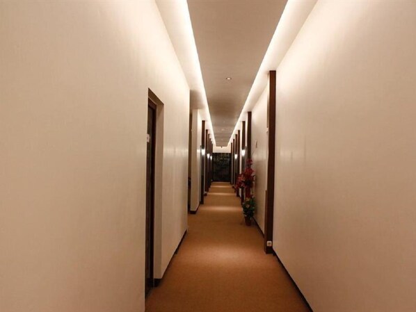 Un lungo e stretto corridoio d'albergo con pavimento rivestito di moquette e pareti bianche.