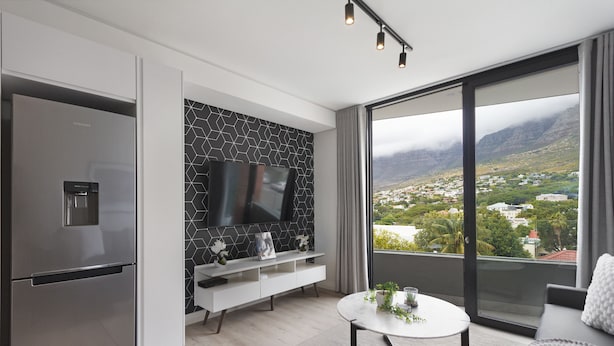 Una cocina moderna con un refrigerador Samsung integrado, un salpicadero de azulejos negros, un televisor de pantalla plana y un amplio ventanal con vistas a un pueblo y montañas.
