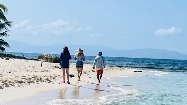 A beach with clear shallow water and a few people walking along the shore.