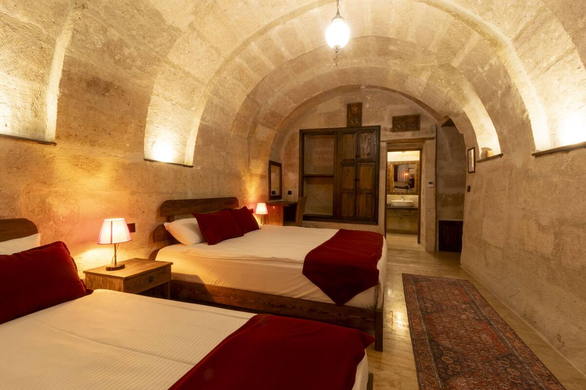 Una habitación con tres camas, cada una con ropa de cama roja y cabeceros de madera, bajo un techo abovedado de piedra.