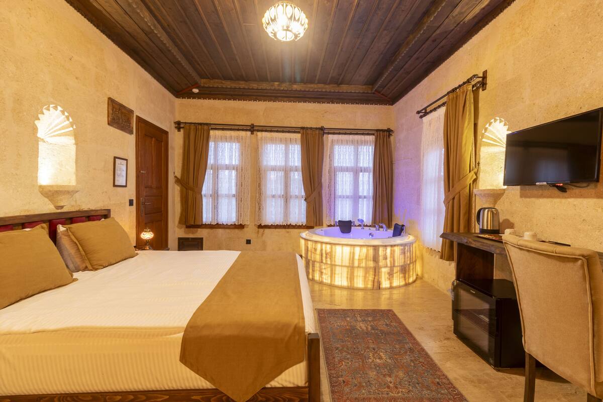 Habitación de hotel con una cama grande, una bañera redonda, un televisor y un escritorio con cafetera.