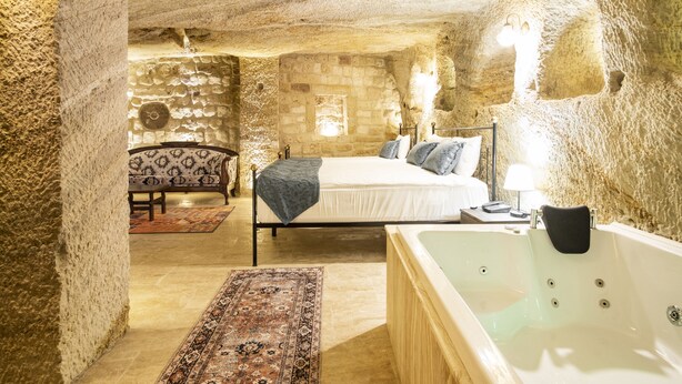A stone-walled bedroom with a bed, a sitting area with a patterned sofa, and a bathtub. - Uzay Cave Suite Hotel (Ürgüp)