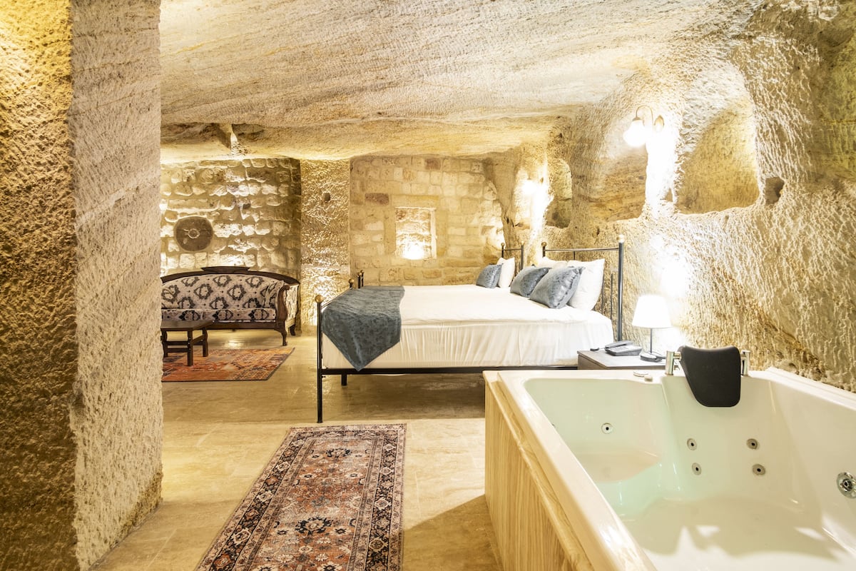 Un dormitorio con paredes de piedra, una cama, una zona de estar con un sofá estampado y una bañera.