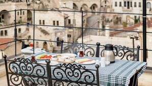 A table with a checkered tablecloth and a metal chair, set against a backdrop of a mountainous landscape with buildings and a hot air balloon in the distance. - Uzay Cave Suite Hotel (Ürgüp)