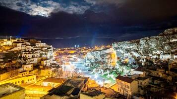 Vista nocturna de un pueblo histórico con edificios iluminados y un acantilado rocoso.