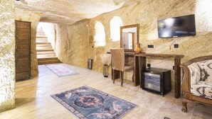 A stone-walled room with a flat-screen TV, a desk, a chair, and a sofa. - Uzay Cave Suite Hotel (Ürgüp)