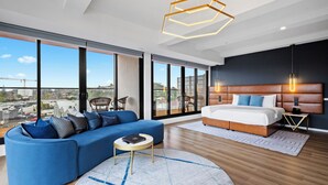 A modern bedroom with a large bed, a blue sofa, and a city view through large windows. - Soho Hotel Auckland (Auckland)