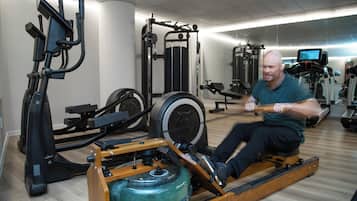 Ein Mann benutzt ein Rudergerät in einem Fitnessstudio mit verschiedenen Trainingsgeräten und einem Spiegel an der Wand.
