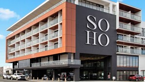 A modern hotel with a prominent 'SOHO' sign, multiple balconies, and a parking area with several cars. - Soho Hotel Auckland (Auckland)