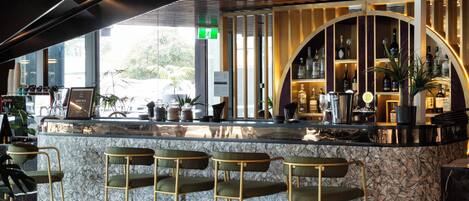 A modern bar area with a marble countertop, bar stools, and a ceiling with exposed ductwork.