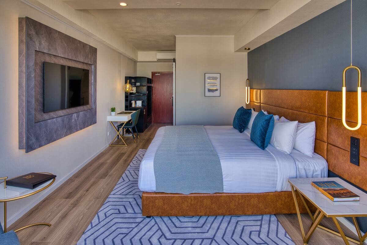 A modern hotel room with a large bed, a desk, and a television mounted on the wall.