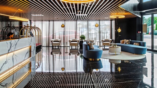 A modern lobby with a reflective floor, a reception desk, seating area, and large windows. - Soho Hotel Auckland (Auckland)