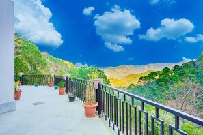 A balcony with potted plants, a black railing, and a view of green hills and a blue sky. - Kia Kasauli Chalet 3 BHK by Dumnu Homes (Krishangarh)