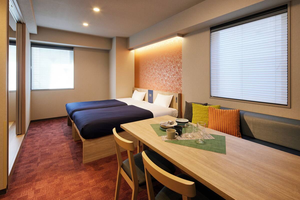 A hotel room with two beds, a dining table, and a sofa.
