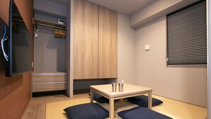 A compact room with a wooden wardrobe, a small table with two cups, and a futon bed with blue cushions. - Minn Nihonbashi (Tokyo)