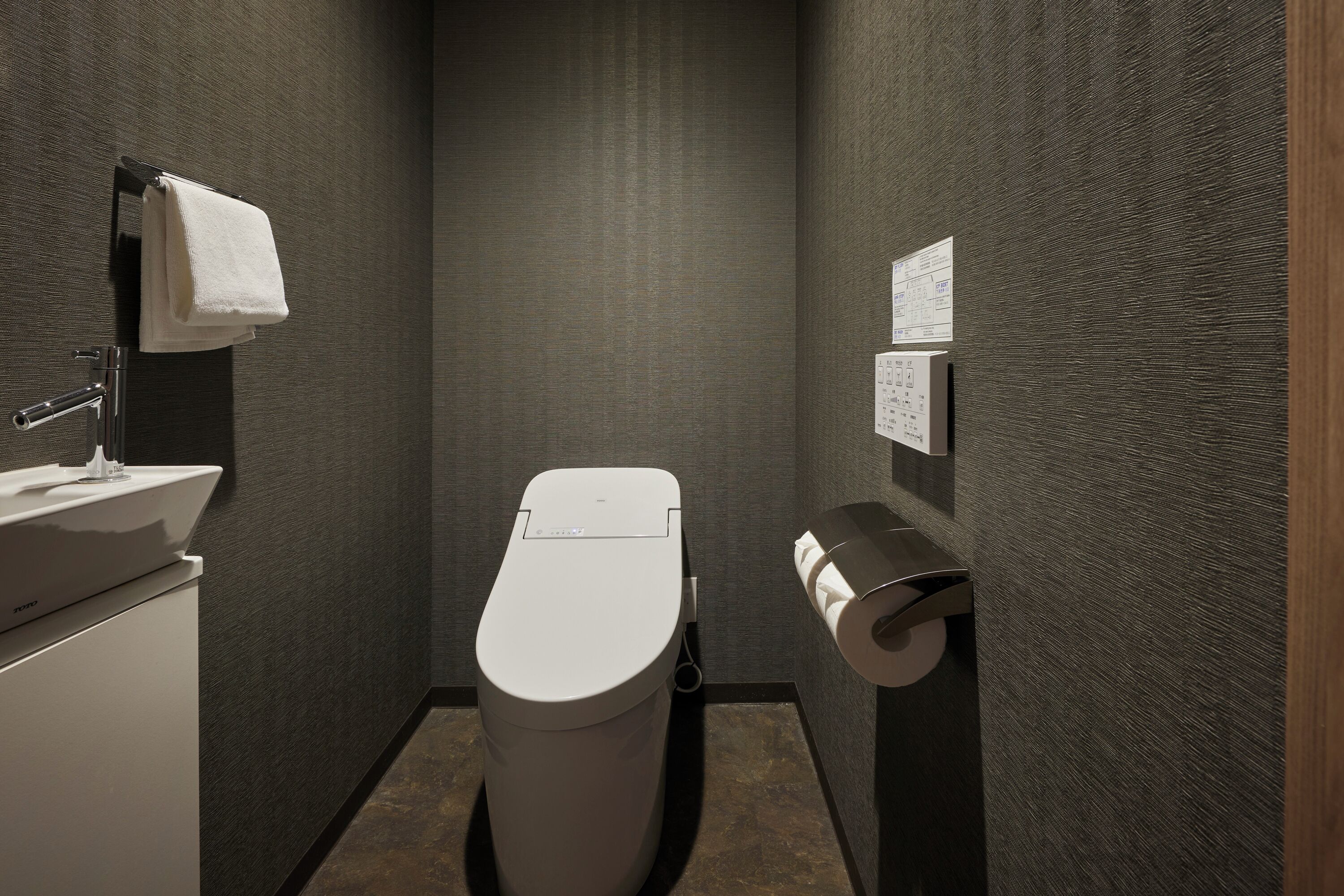 A compact bathroom with a toilet, a sink, and a paper towel dispenser.