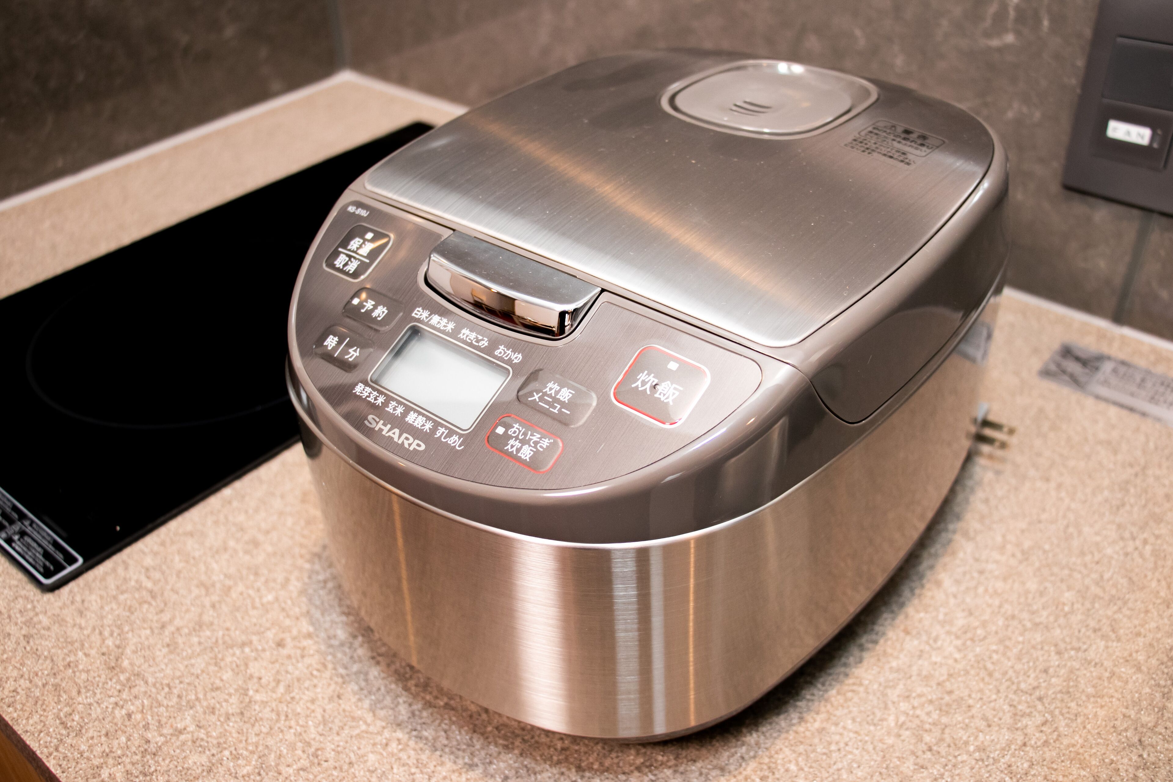 A modern kitchen with a stainless steel appliance, a digital control panel, and a black induction cooktop.