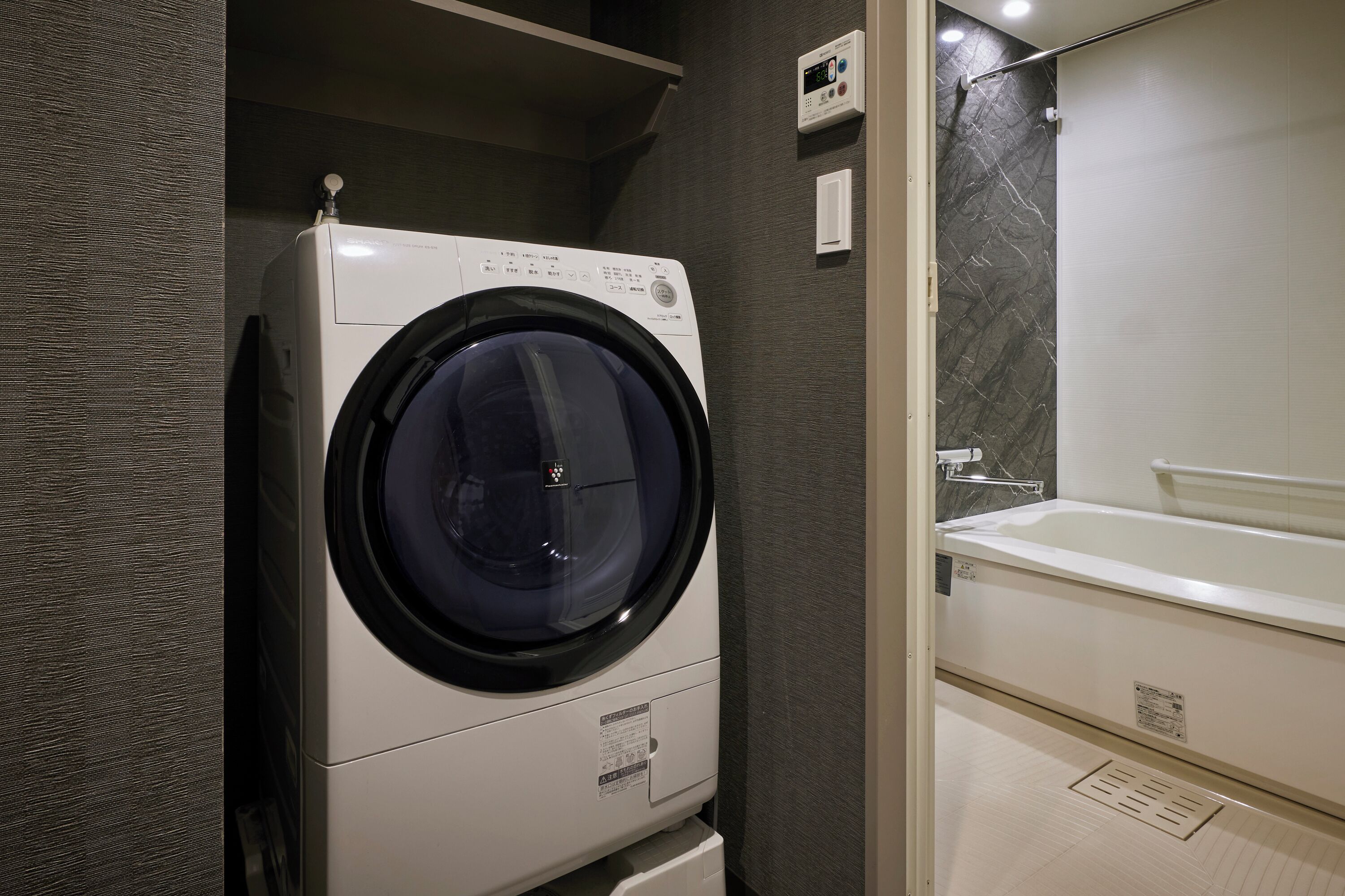 A modern bathroom with a built-in washer and dryer, a marble-tiled shower, and a large mirror.