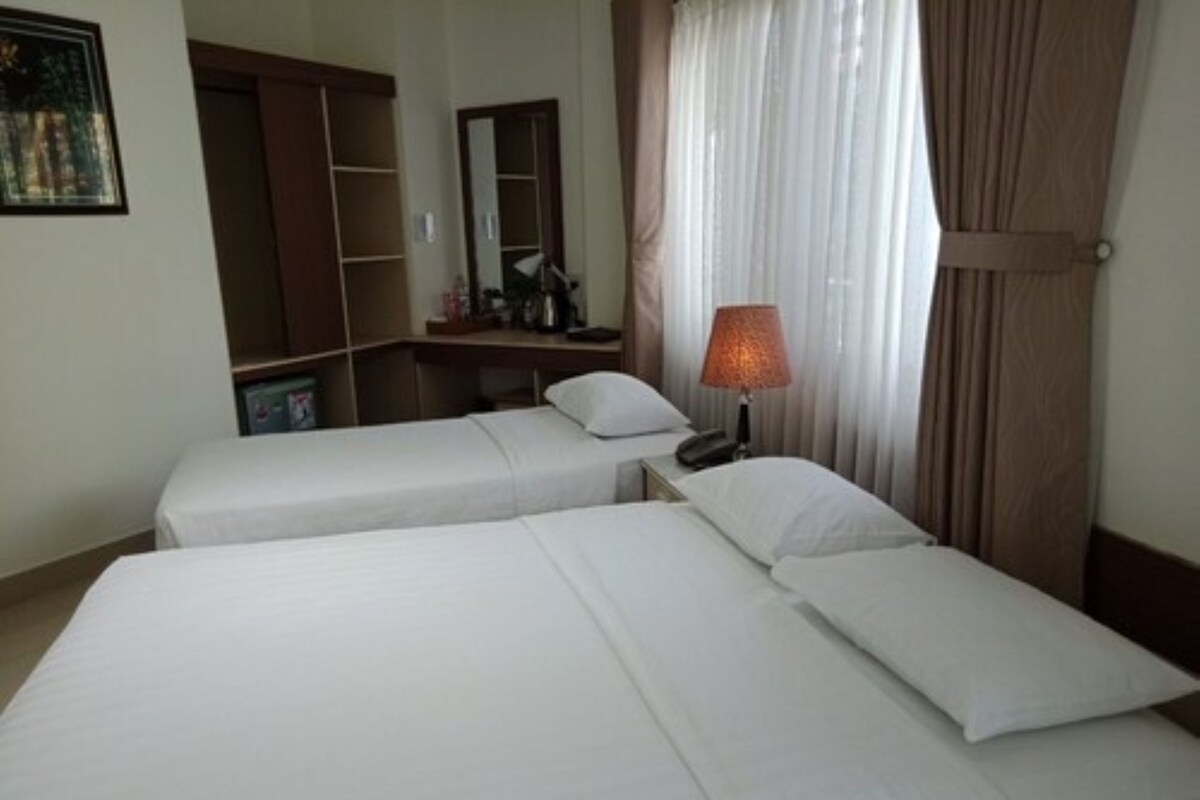 A hotel room with two single beds, a bedside table with a lamp, a wardrobe, and a mirror.