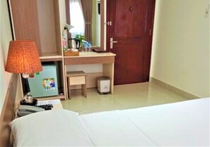 A hotel room with a bed, a desk, a lamp, a mirror, and a door. - An Hotel by Zuzu (Can Tho Municipality)