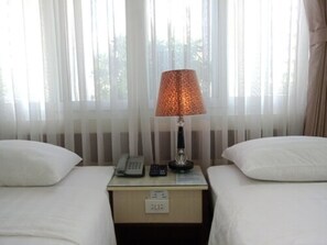 Une chambre d’hôtel avec deux lits, une table de chevet avec une lampe, un téléphone et un petit tiroir.