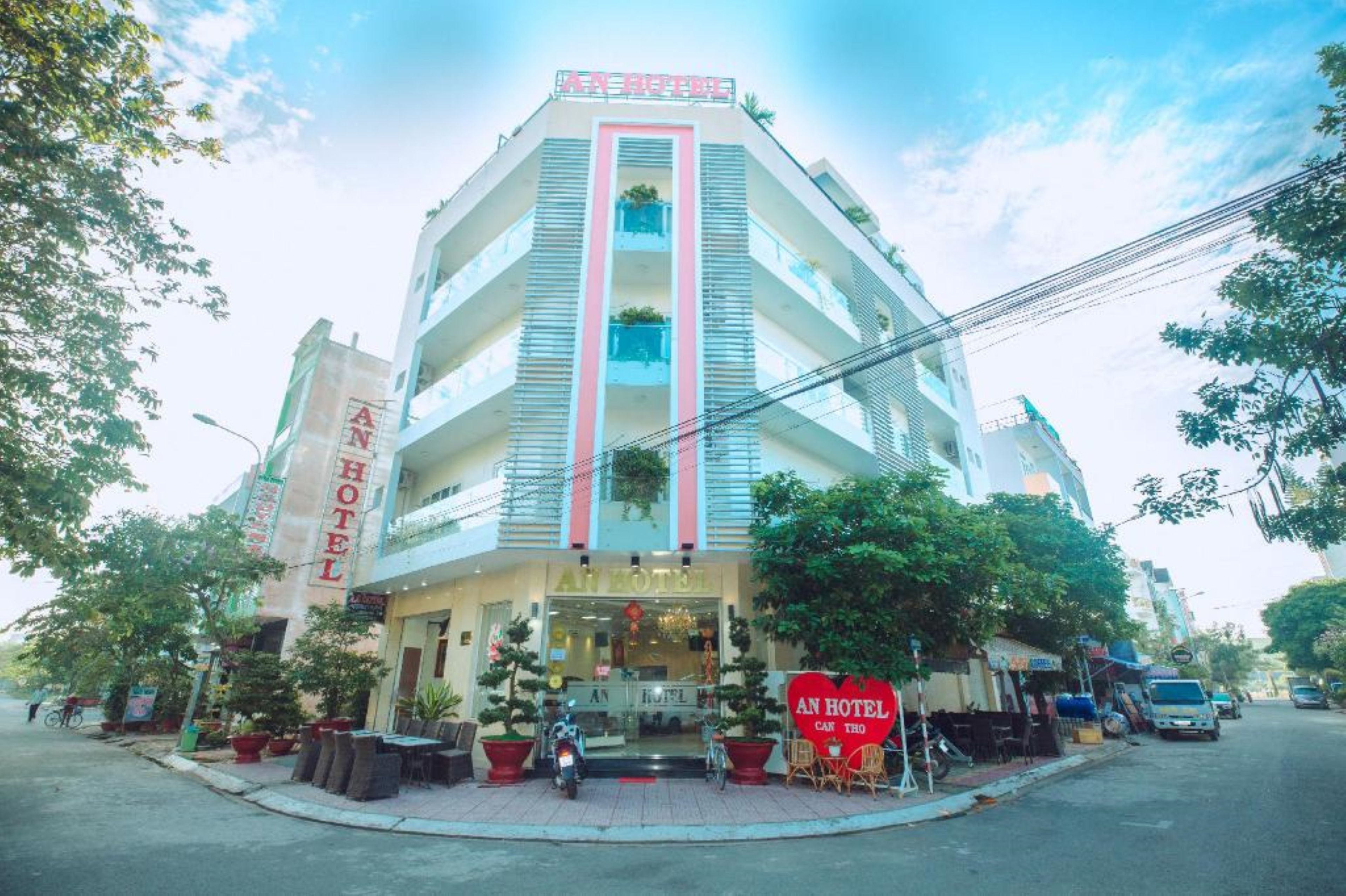 A multi-story hotel with a prominent vertical sign, outdoor seating, and potted plants.
