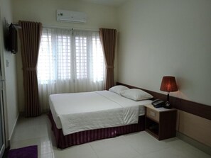 A hotel room with a bed, curtains, a bedside table with a lamp, and an air conditioning unit. - An Hotel by Zuzu (Can Tho Municipality)